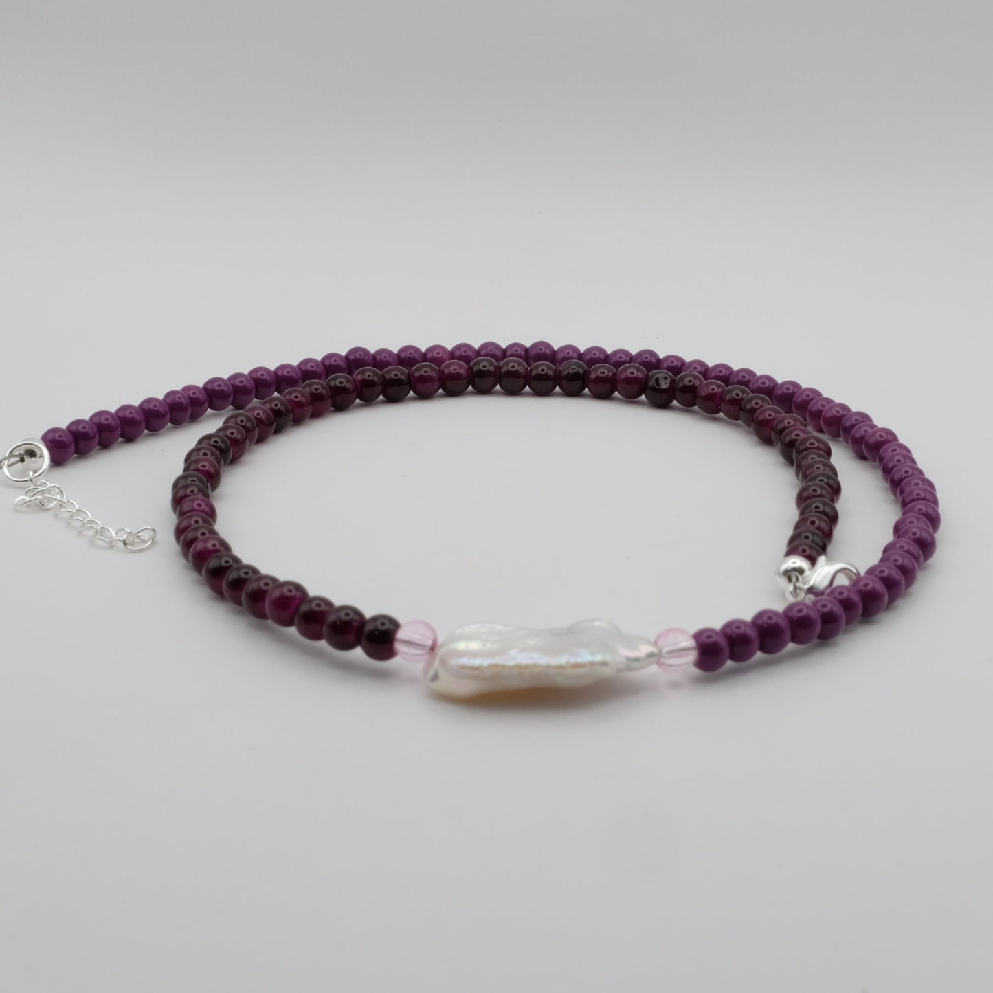 Purple beaded bracelet with a clear crystal bead on a light gray background