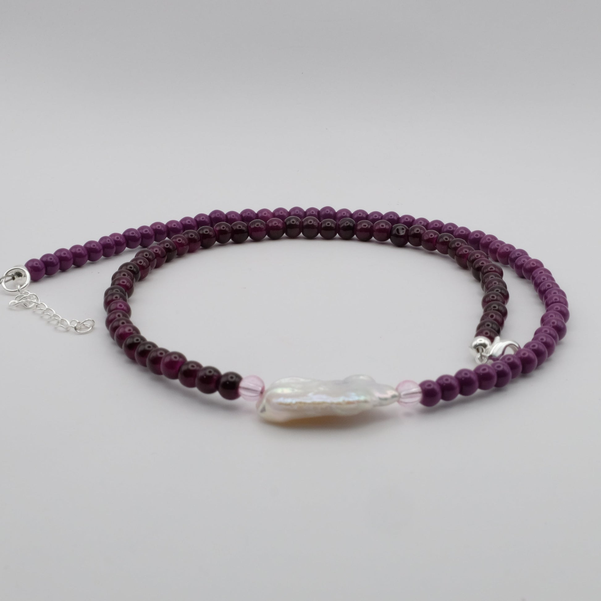 Purple beaded bracelet with a clear crystal bead on a light gray background
