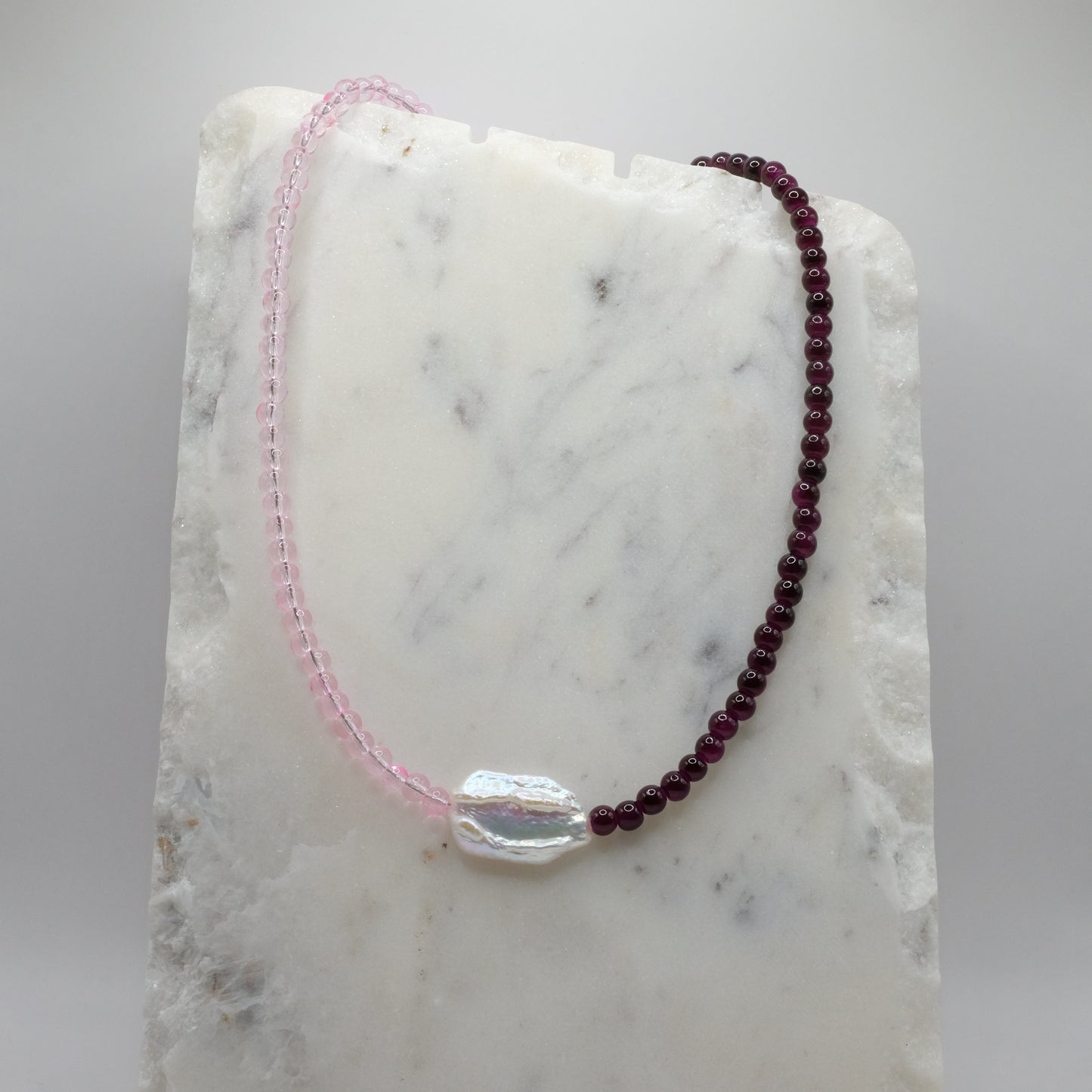 Beaded necklace with pink and red beads on a marble surface
