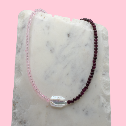 Beaded necklace with pink and purple beads on a marble surface with a pink background