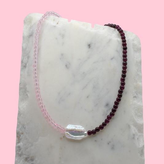 Beaded necklace with pink and purple beads on a marble surface with a pink background