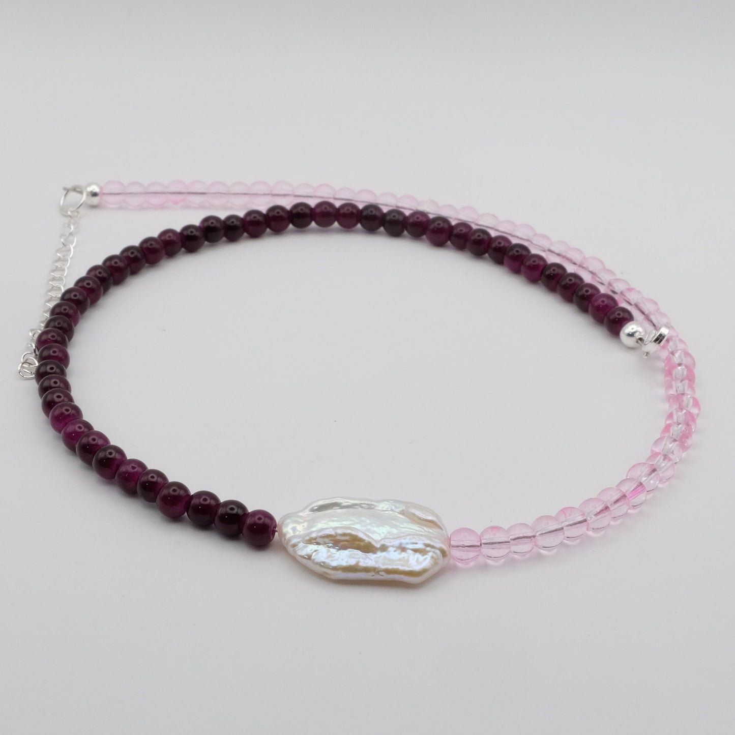 A handmade beaded necklace featuring 4mm light pink glass beads on one side, 4mm deep purple glass beads on the other, and a white baroque freshwater pearl centrepiece, displayed on a white background.