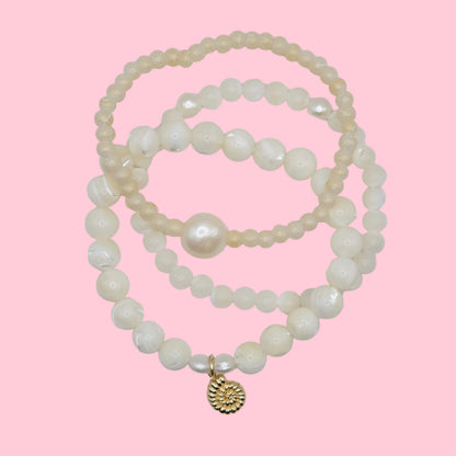 Stack of mother of pearl and pearl bracelets with a gold nautilus seashell charm on a pink background