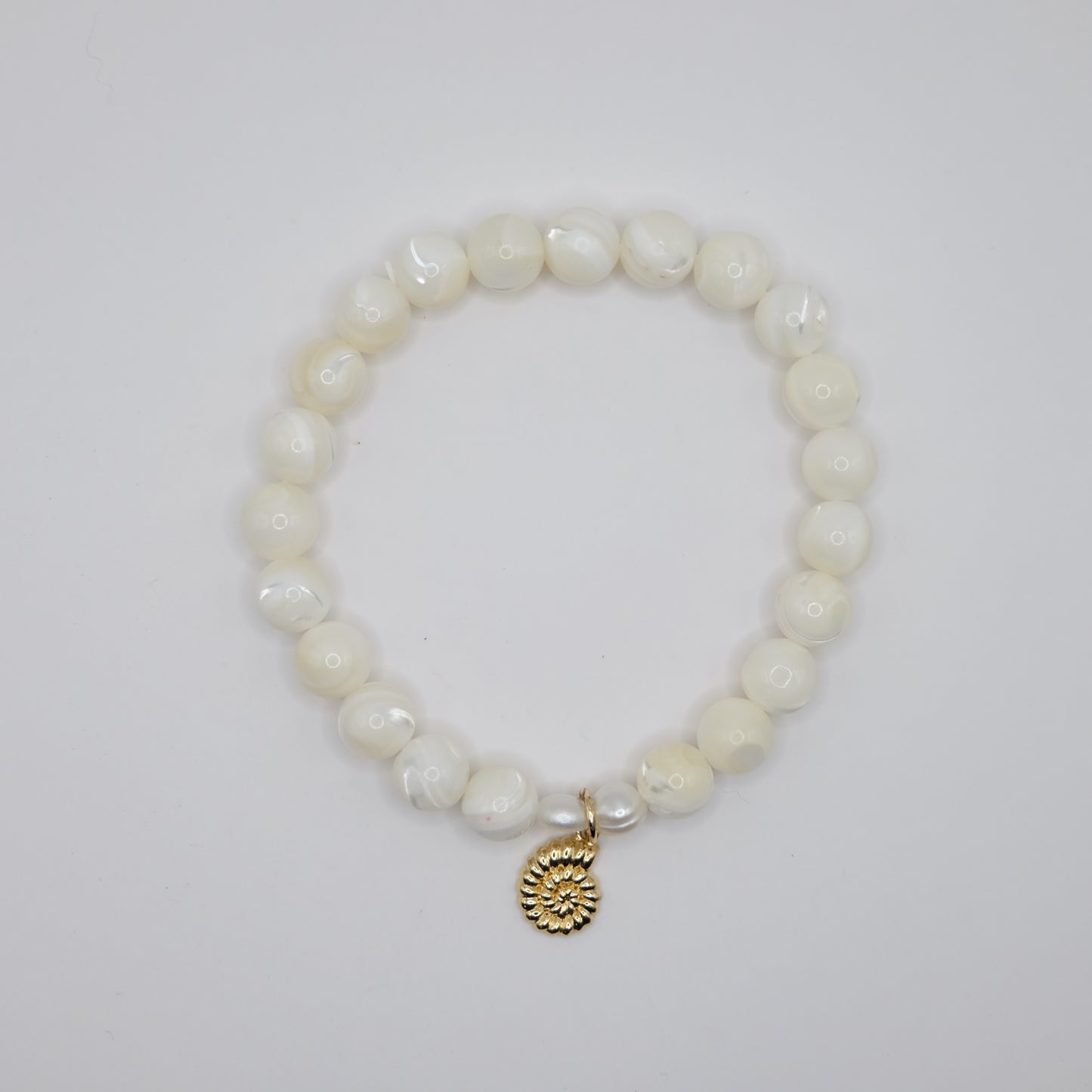 Pearl bracelet with a gold charm on a light gray background