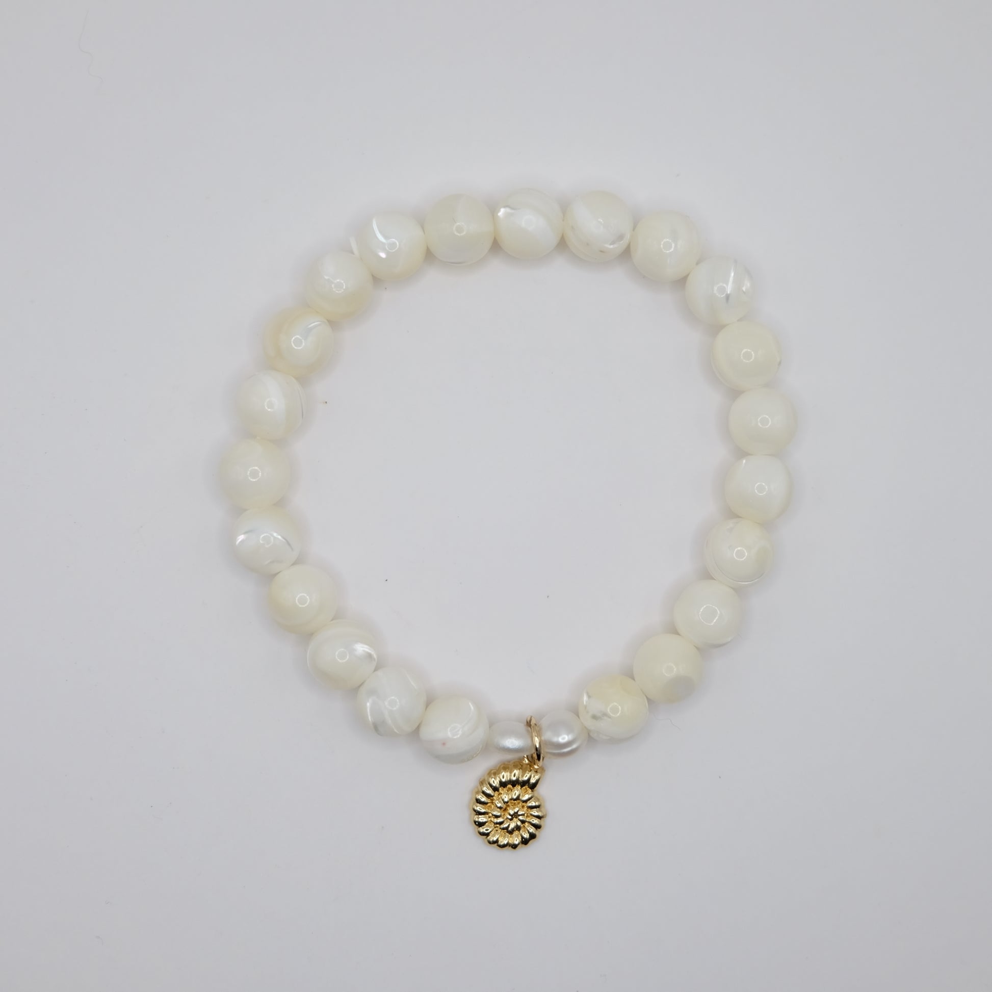 Pearl bracelet with a gold charm on a light gray background