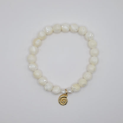 Pearl bracelet with a gold charm on a light gray background
