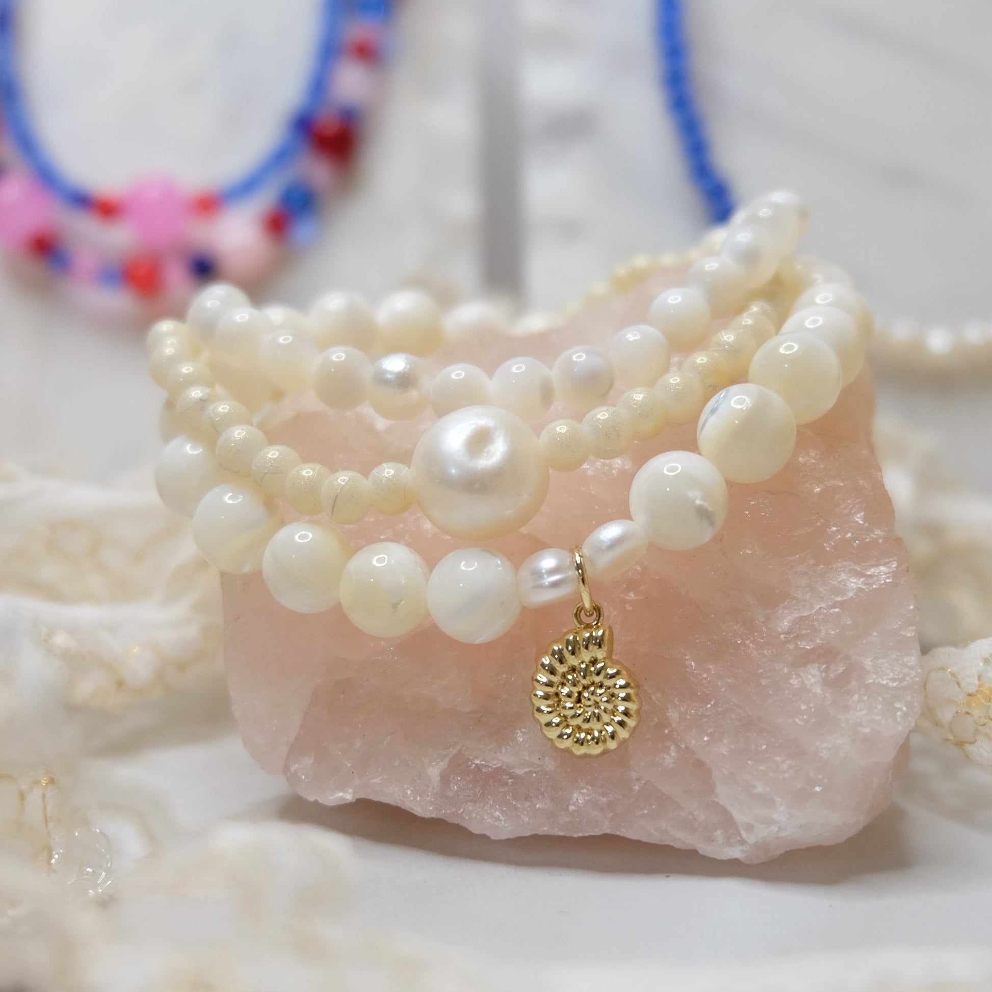 Stack of pearl bracelets with a gold charm on a stone surface