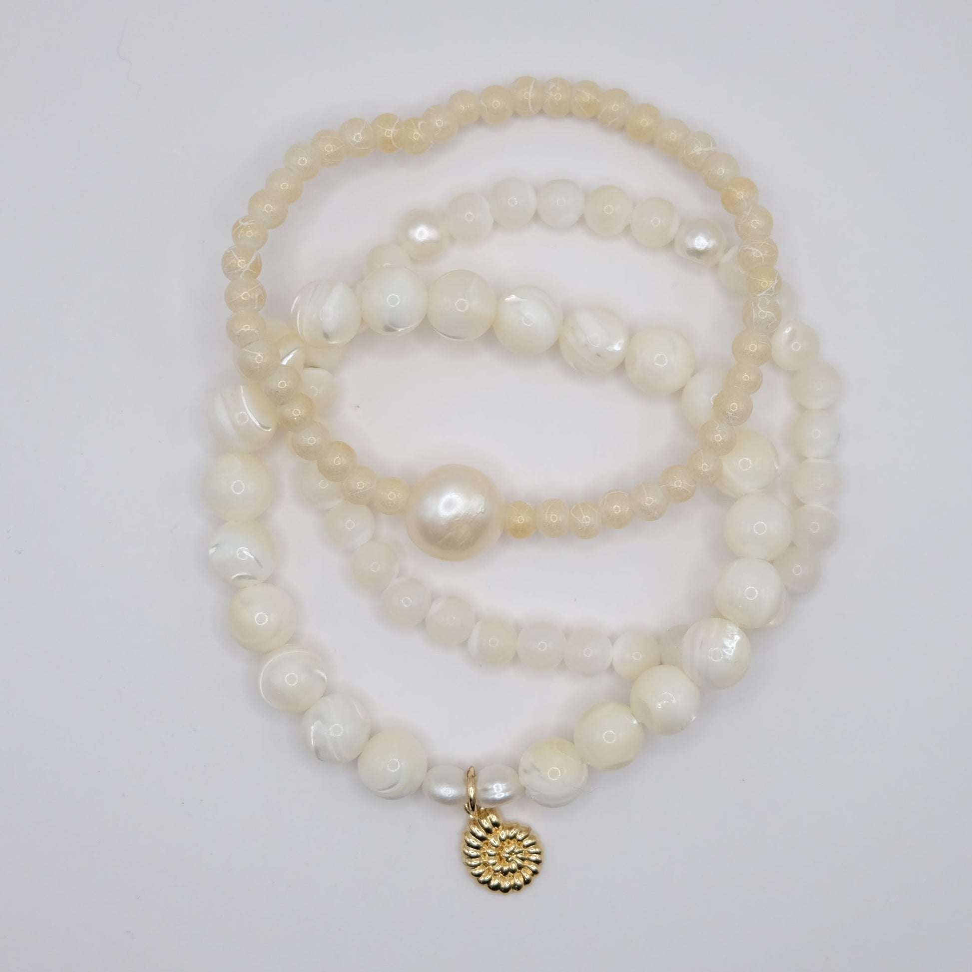 Stack of pearl bracelets with a gold charm on a light gray background