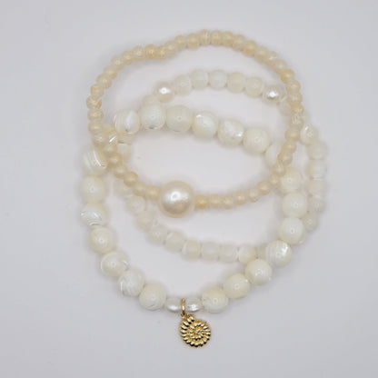 Stack of pearl bracelets with a gold charm on a light gray background