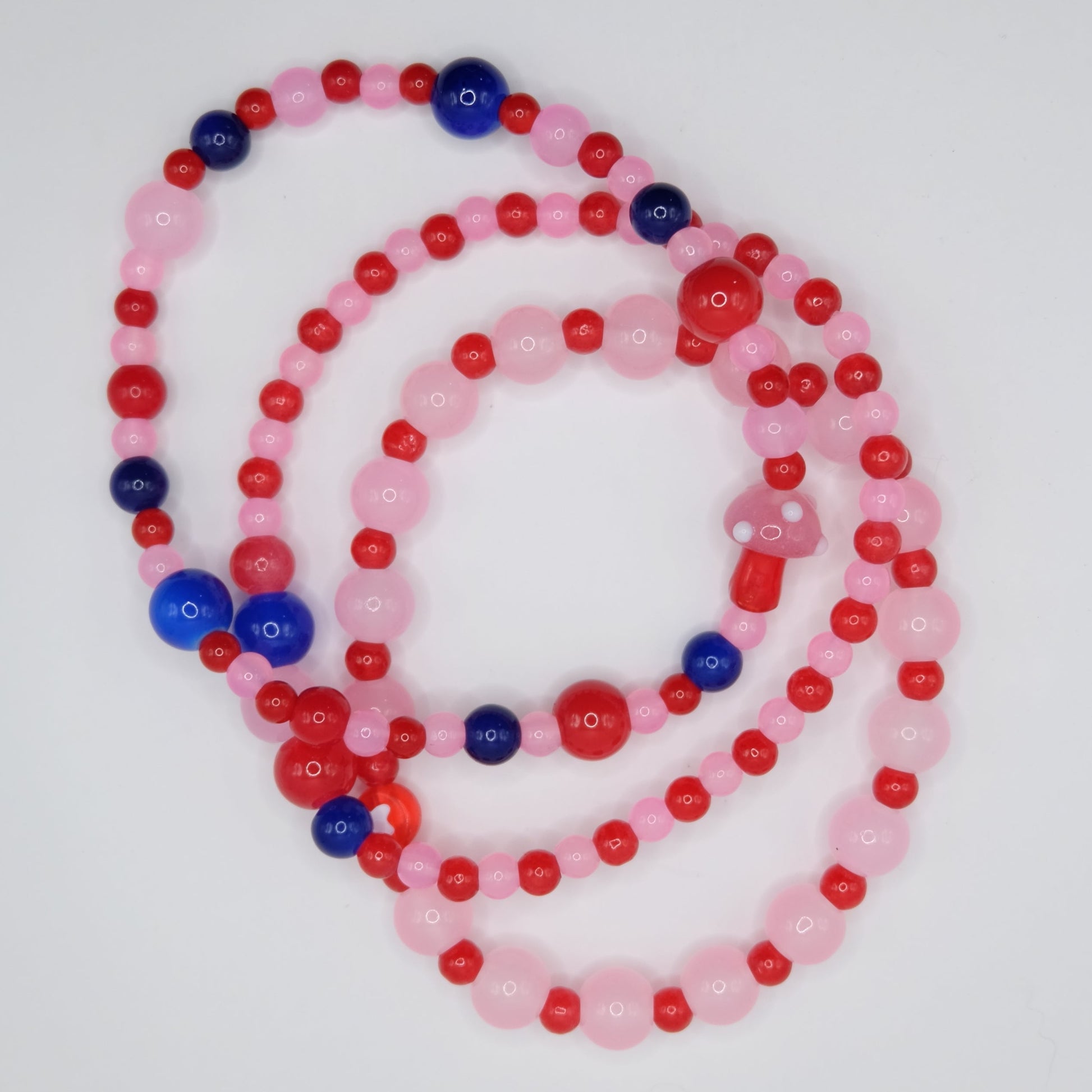 Beaded bracelets with pink, red, and blue beads on a pink background