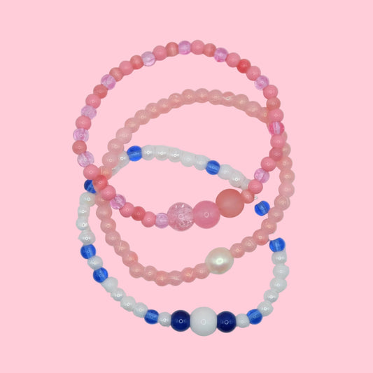 A colourful elastic beaded bracelet stack with mixed glass beads in pink, red and blue, featuring varied sizes and finishes.