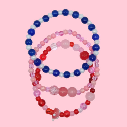 A one of a kind elastic jewellery stack made from mixed glass beads in pink, red and blue tones, designed as a bold layered set.