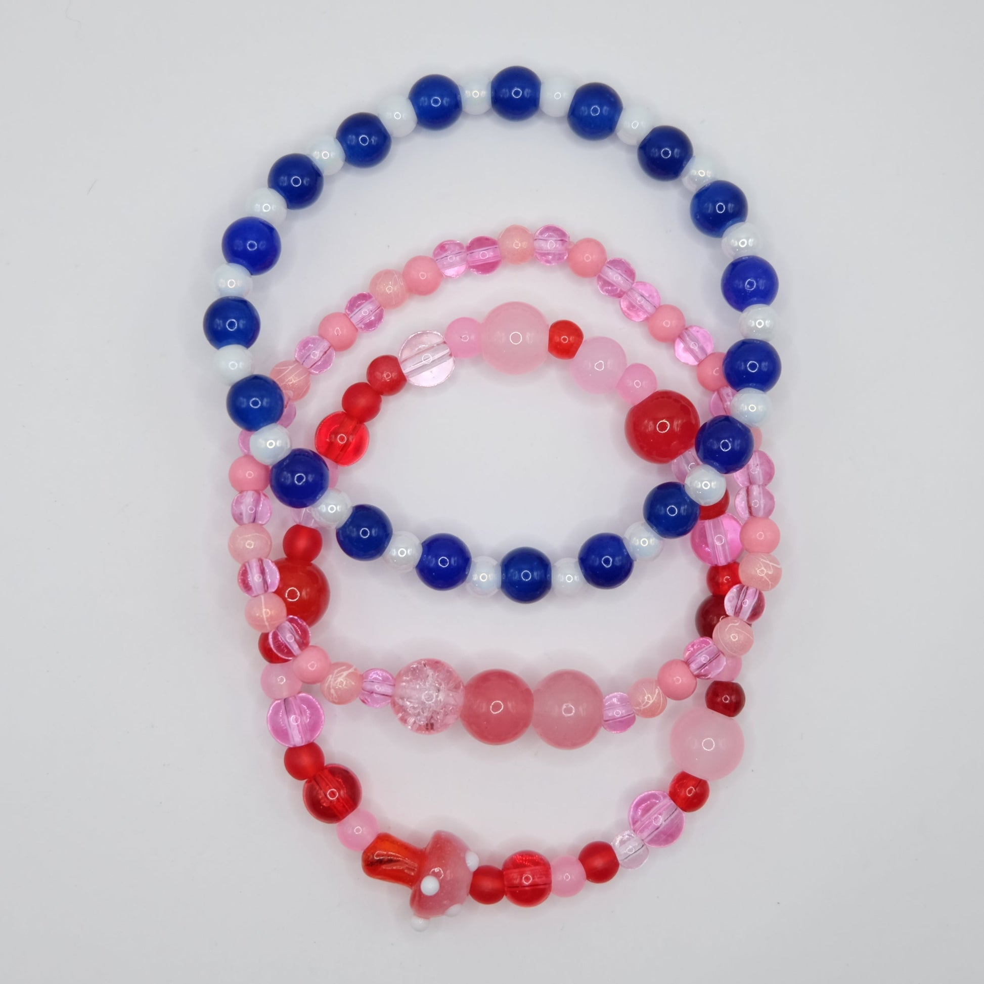 Set of 3 colorful glass beaded bracelets  in pinks, reds and blue tones on a plain background
