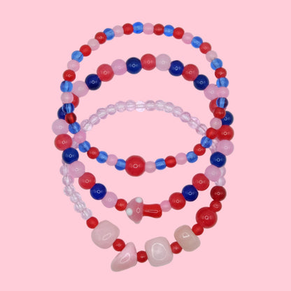 A handmade bracelet stack composed of colourful glass beads in varying sizes, blending pink, red and blue tones in a layered trio.