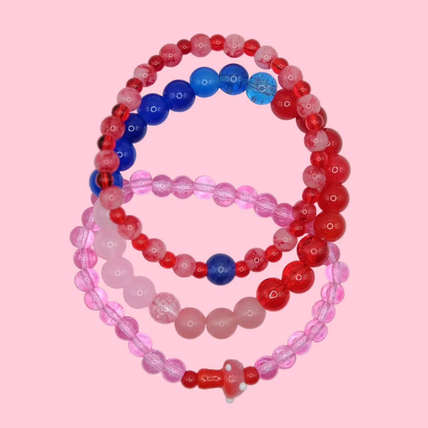 A vibrant bracelet stack featuring mixed size glass beads in pink, red and blue tones, styled as a layered elastic set.
