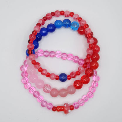 Set of three beaded bracelets in red, blue, and pink on a light gray background