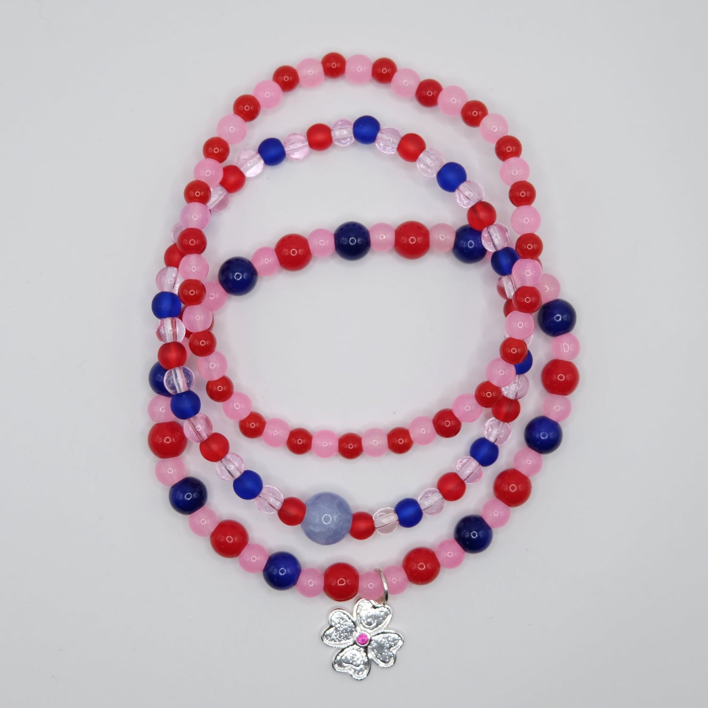 Beaded bracelet stack with red, blue, and pink beads on a plain background