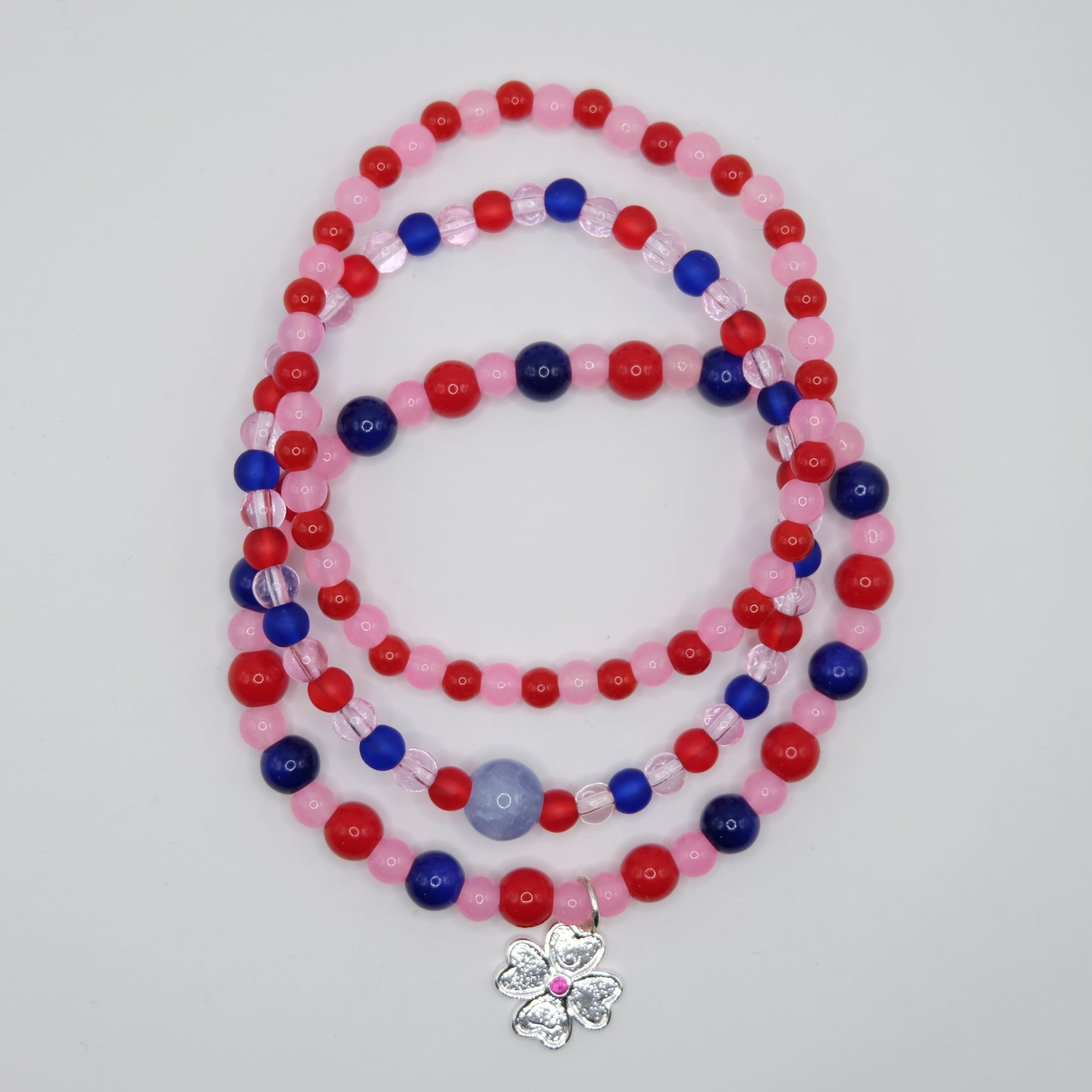Beaded bracelet stack with red, blue, and pink beads on a plain background