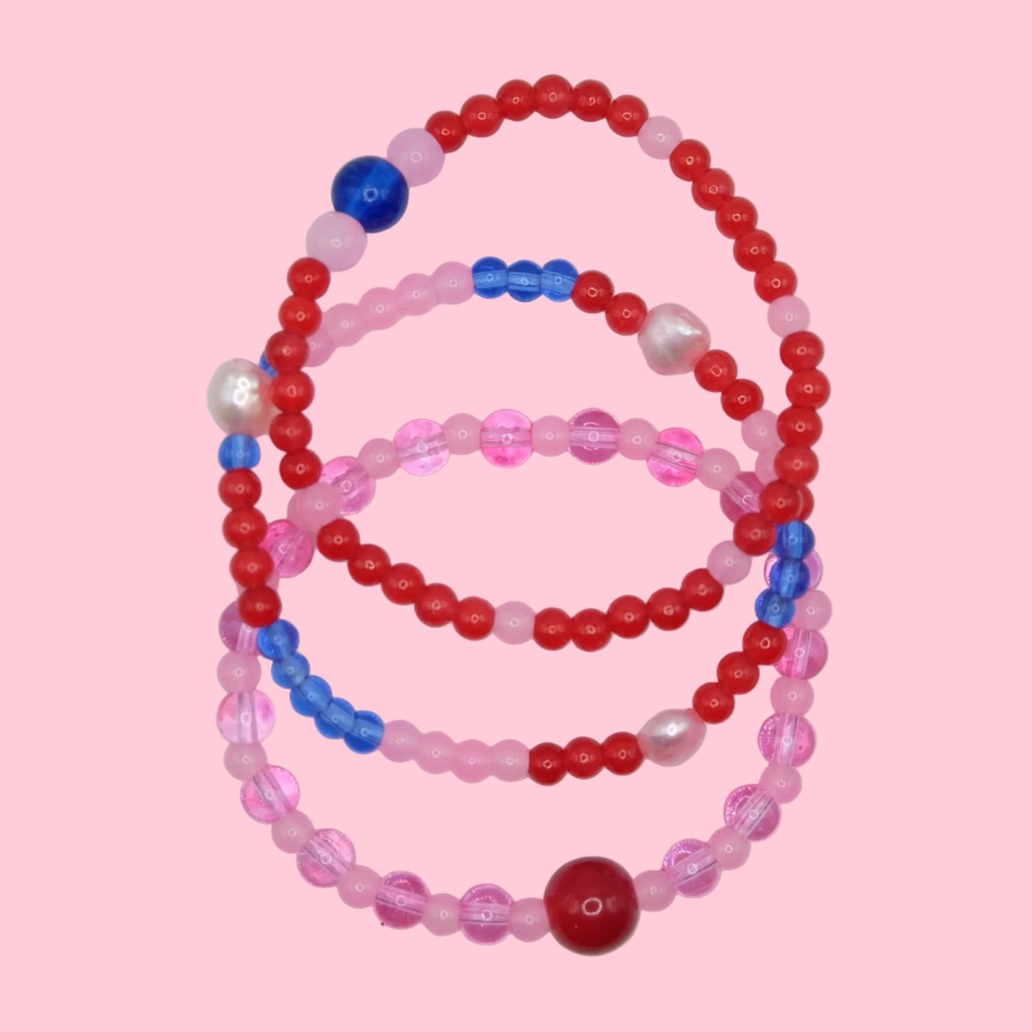 A unique beaded bracelet stack OF 3 made from mixed 4mm to 8mm glass beads in pink, red and blue hues, designed for layering.