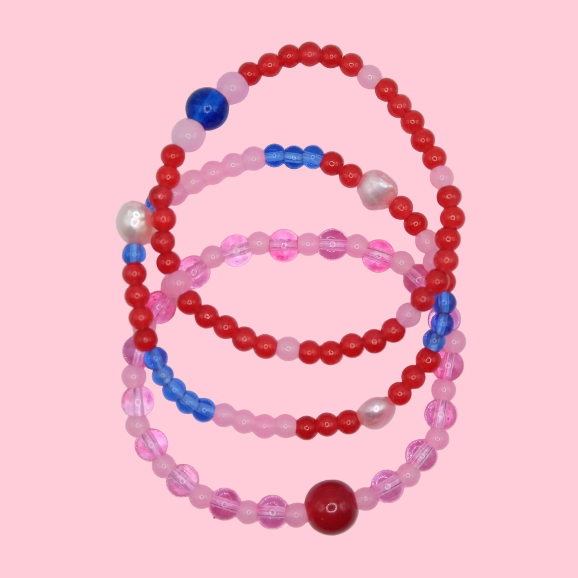 A unique beaded bracelet stack OF 3 made from mixed 4mm to 8mm glass beads in pink, red and blue hues, designed for layering.