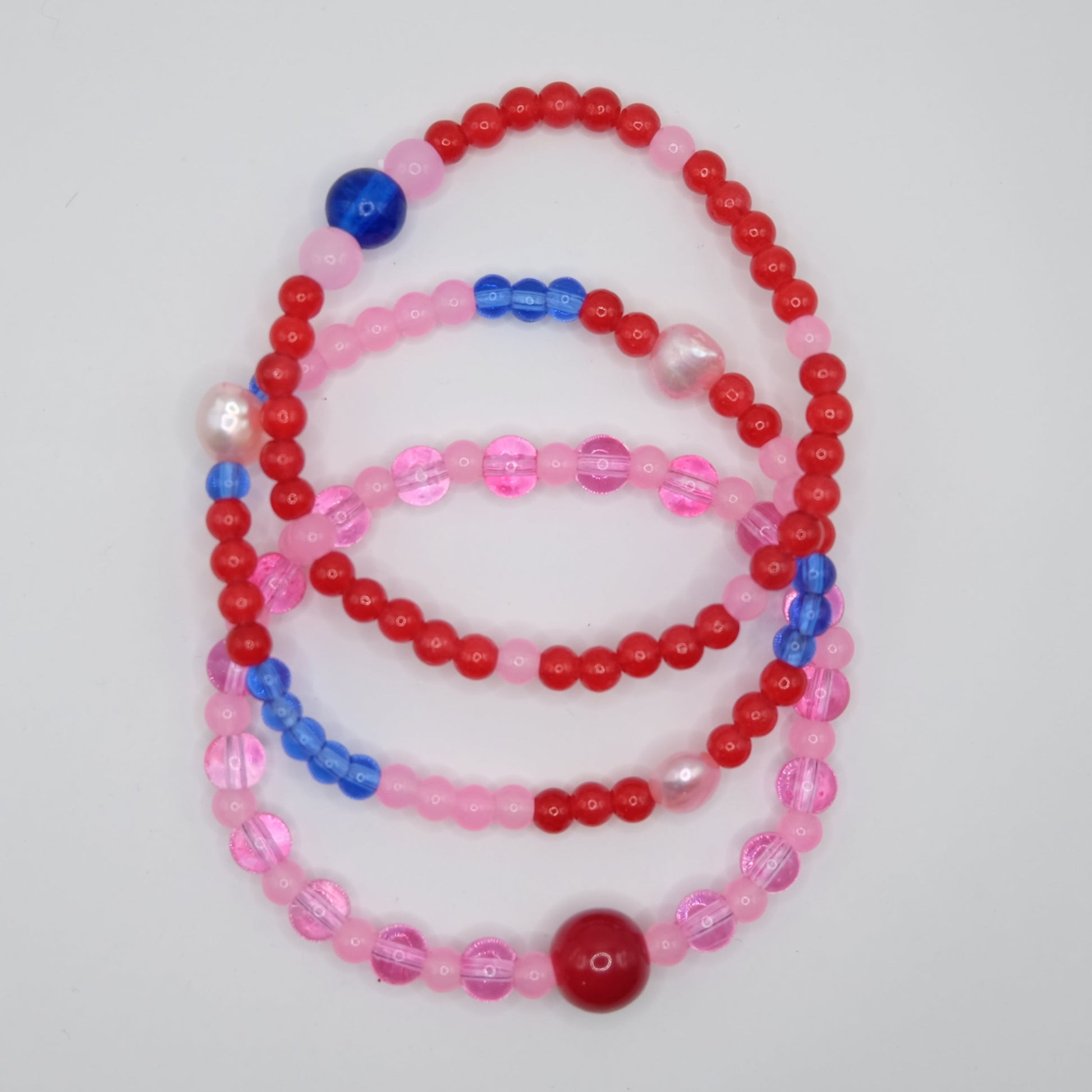 Set of three beaded necklaces in red, pink, and blue on a light gray background