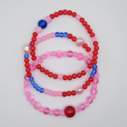Set of three beaded necklaces in red, pink, and blue on a light gray background