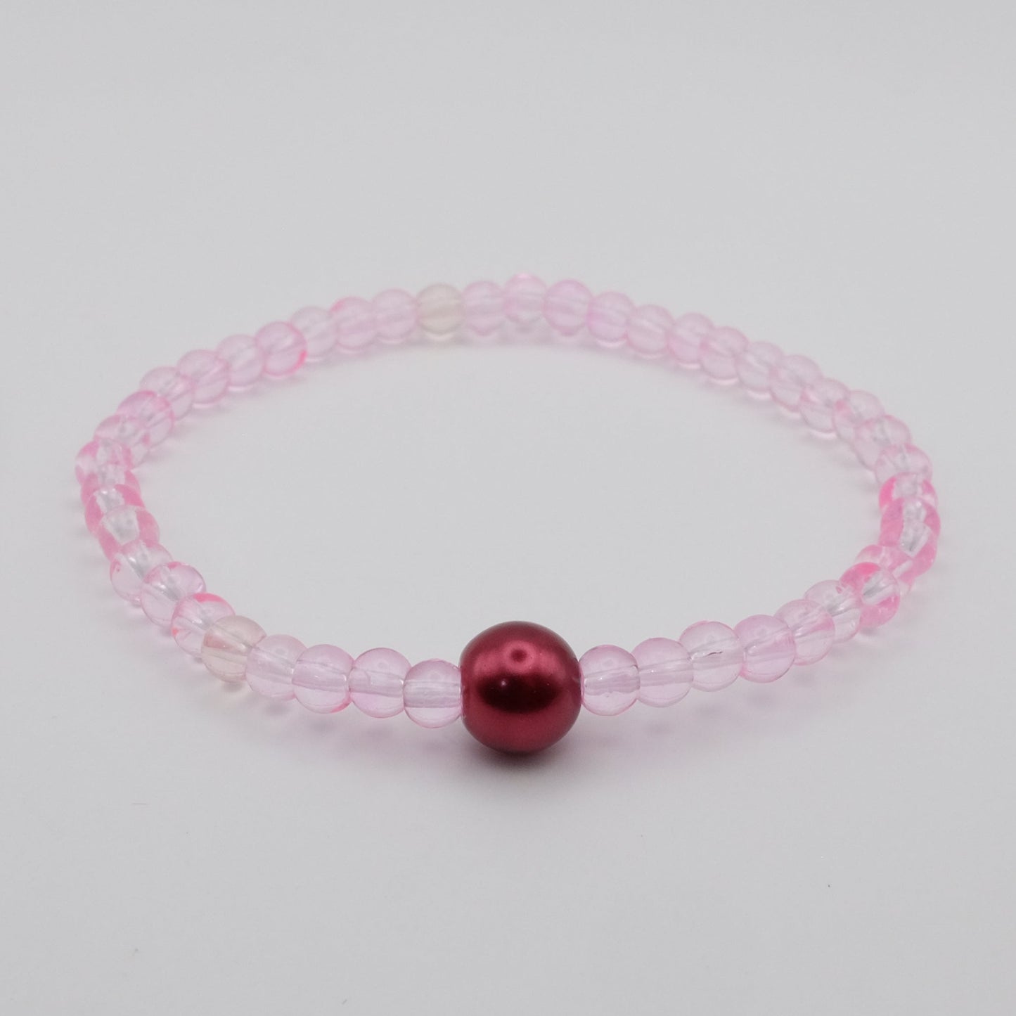 Pink beaded bracelet with a red bead on a light gray background
