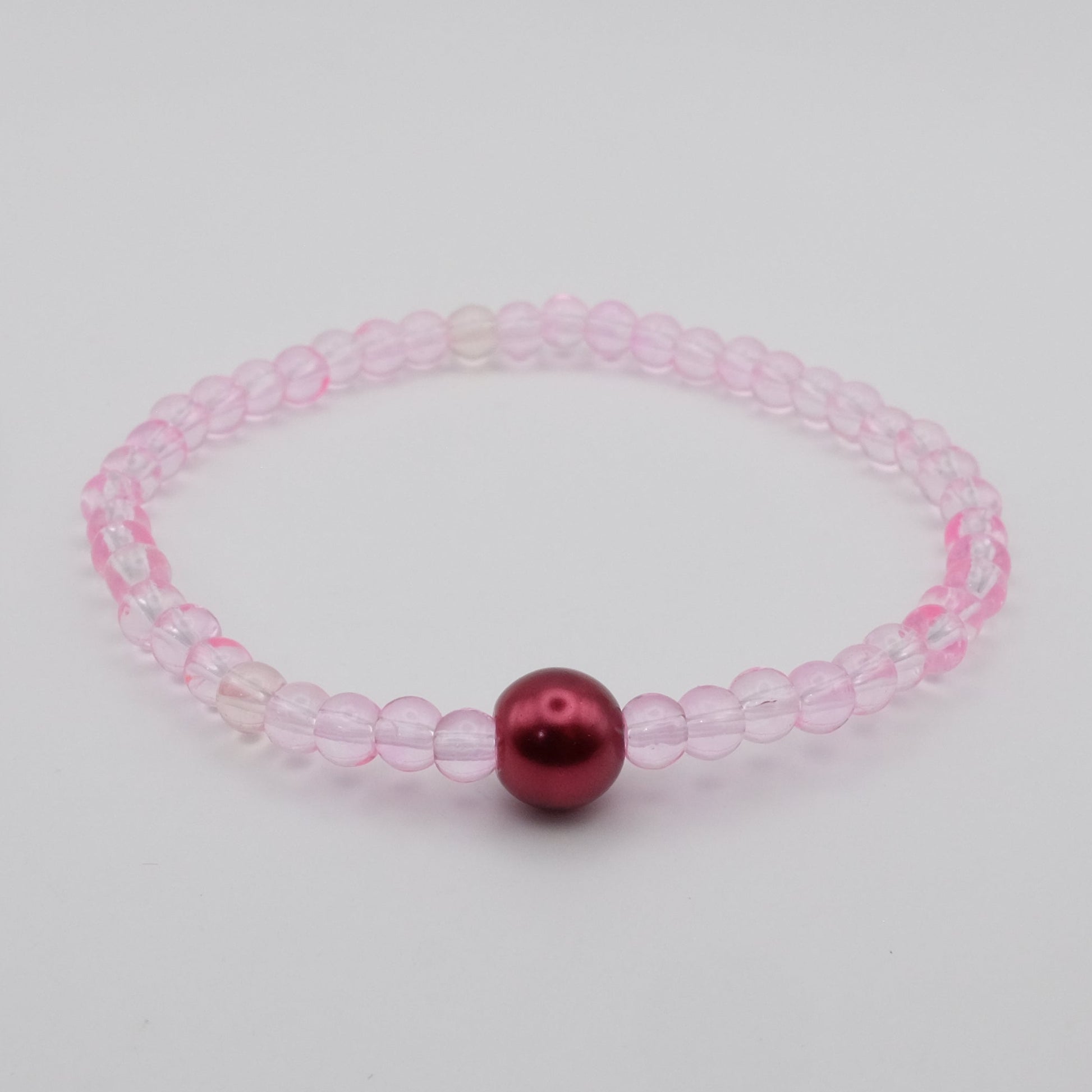 Pink beaded bracelet with a red bead on a light gray background