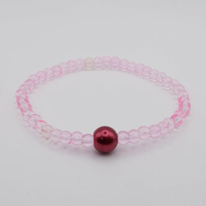 Pink beaded bracelet with a red bead on a light gray background
