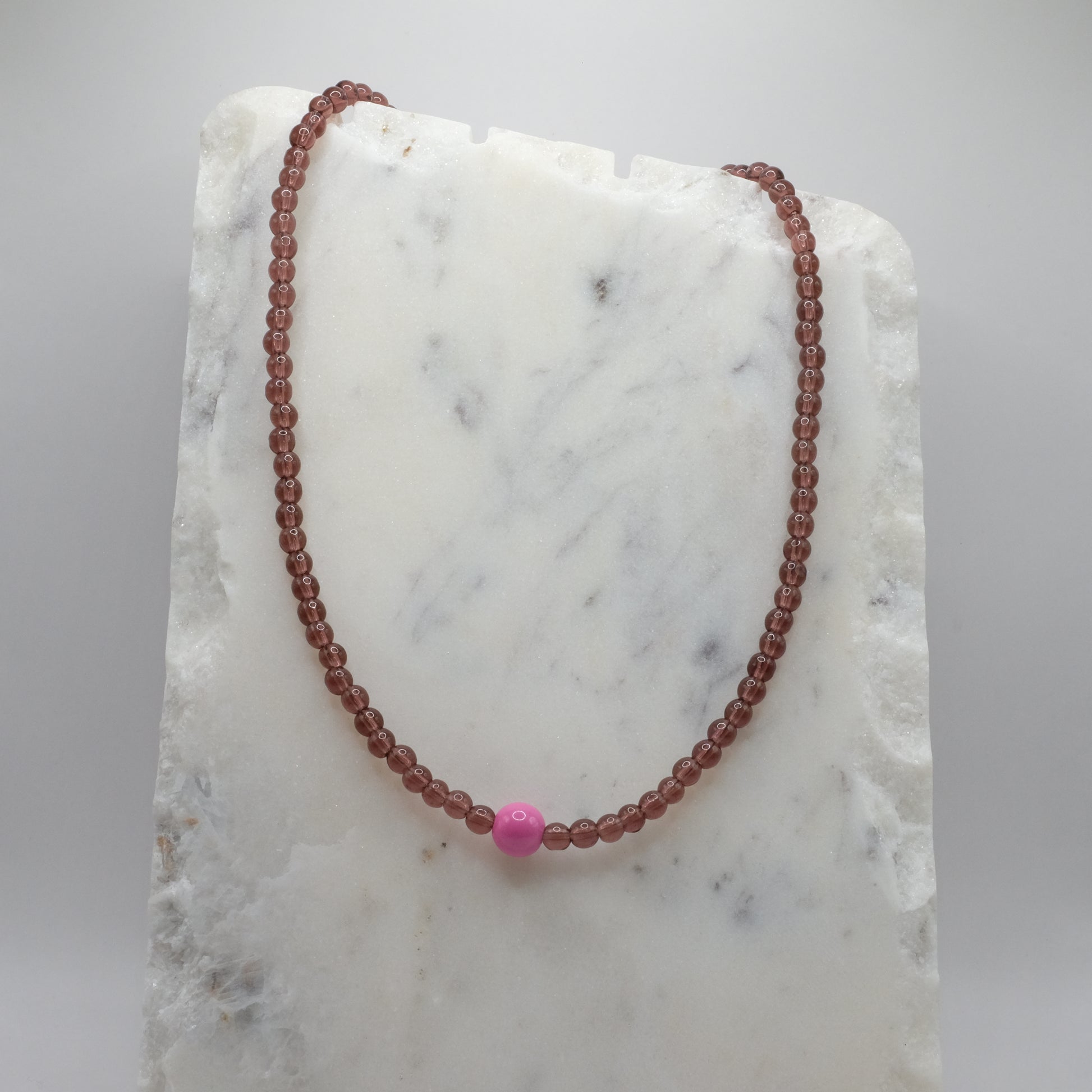 Beaded necklace with a pink bead on a marble surface