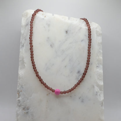 Beaded necklace with a pink bead on a marble surface