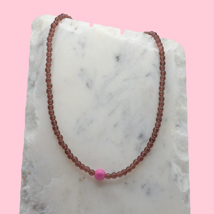 Beaded necklace with a pink bead on a marble surface with a pink background