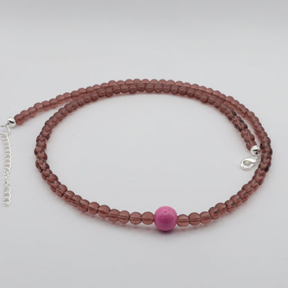 A handmade beaded necklace composed of 4mm light burgundy glass beads with a single 8mm pink feature bead at the centre, displayed on a white background.