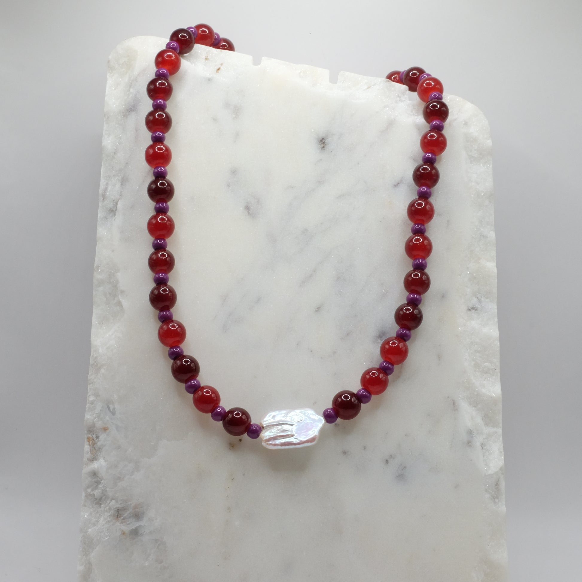 Beaded necklace with red and purple beads on a marble surface