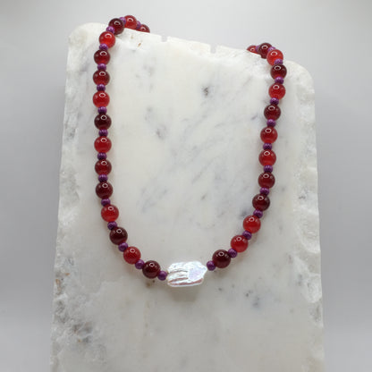 Beaded necklace with red and purple beads on a marble surface