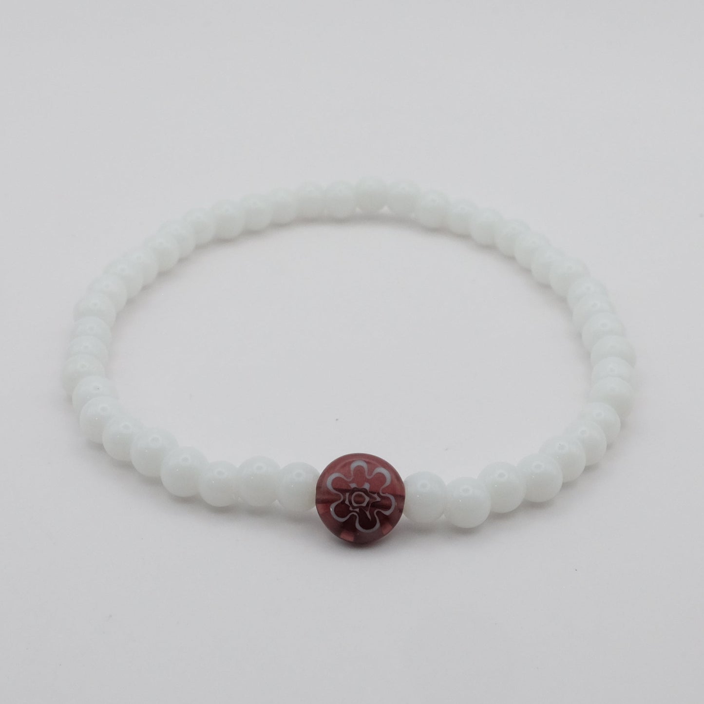 White bracelet with a purple flower charm on a light gray background