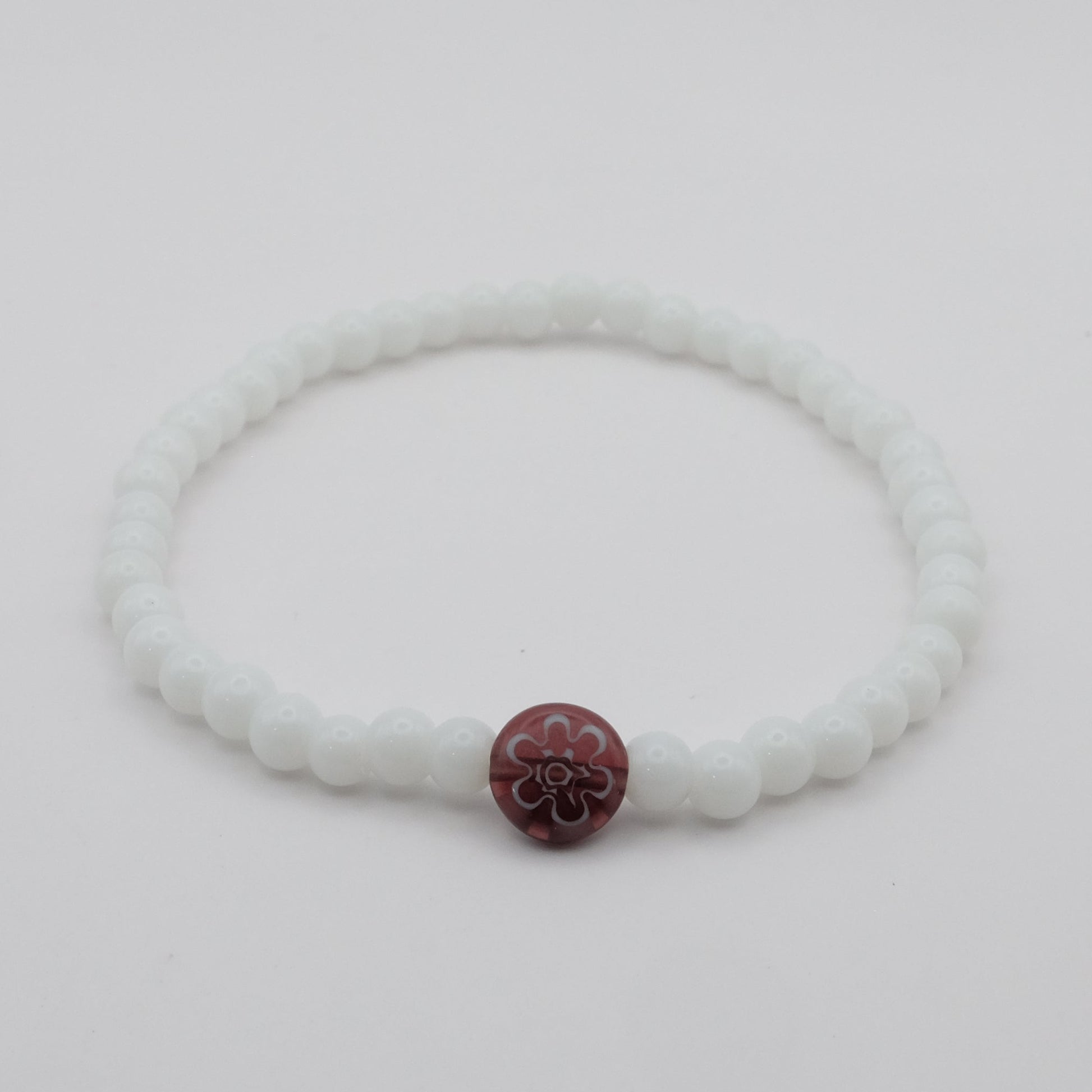 White bracelet with a purple flower charm on a light gray background
