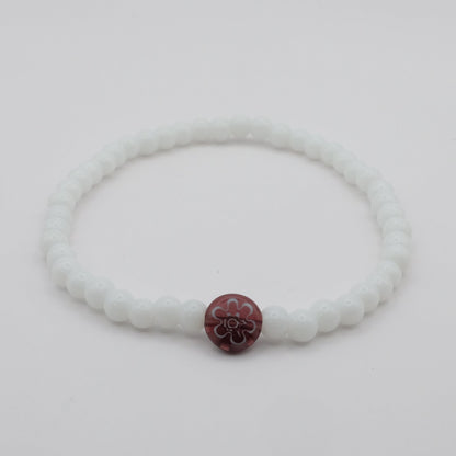 White bracelet with a purple flower charm on a light gray background