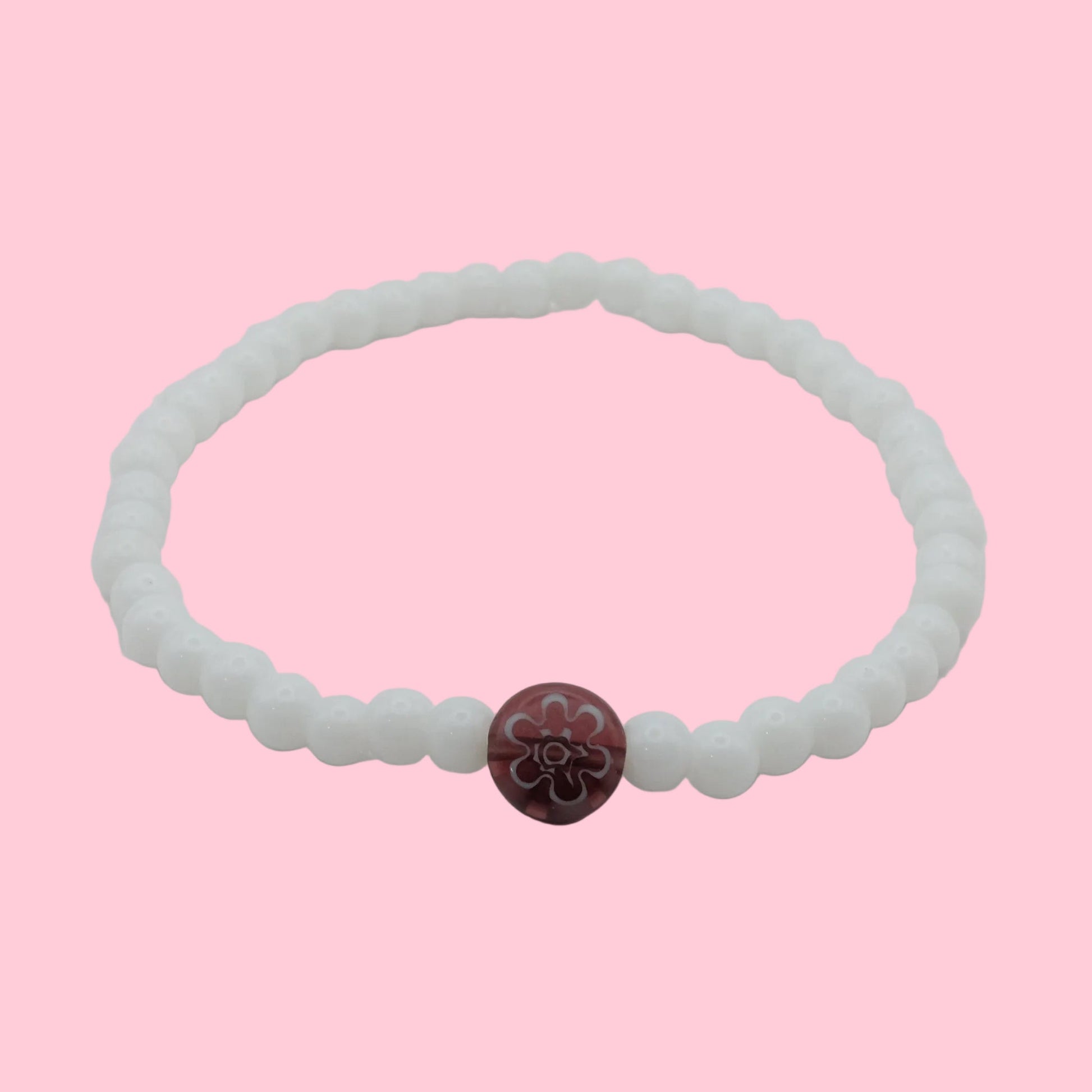 An elastic beaded bracelet composed of glossy white 4mm glass beads featuring a single plum floral lampwork bead at the centre, shown on a white background.
