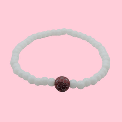 An elastic beaded bracelet composed of glossy white 4mm glass beads featuring a single plum floral lampwork bead at the centre, shown on a white background.