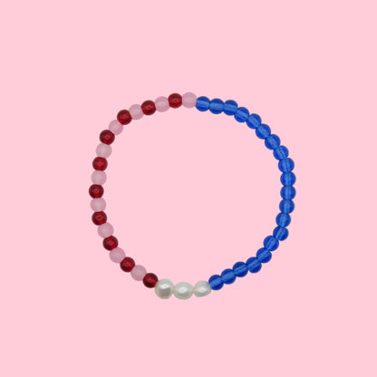 An elastic beaded bracelet composed of 4mm glass beads - half blue and half alternating red and pink, featuring three freshwater pearl accents, shown on a pink background.