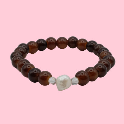 An elastic beaded bracelet composed of 6mm translucent cocoa and chestnut brown glass beads, featuring a freshwater pearl focal bead framed by clear accent beads, shown on a clean white background.
