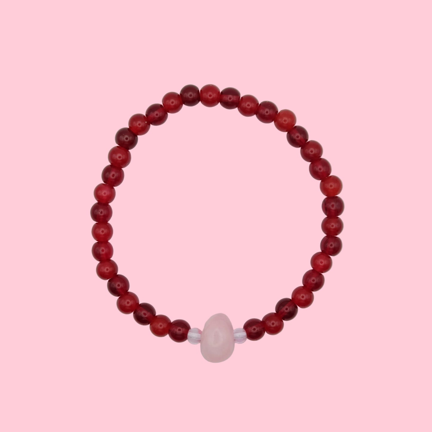 An elastic beaded bracelet composed of 6mm glass beads in shade of red tones - featuring a central pink dyed jade bead framed by smaller glass beads, shown on a pink background.