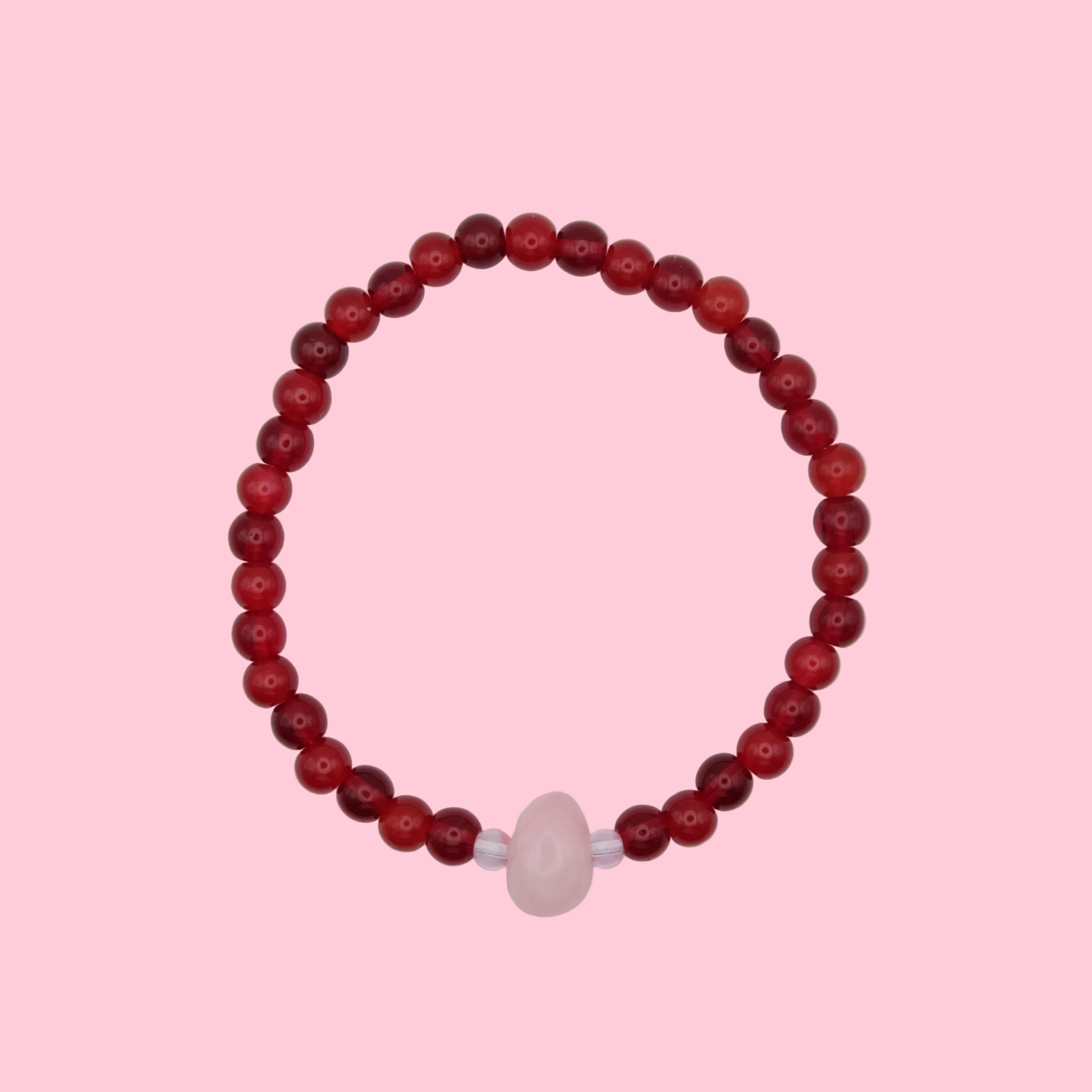 An elastic beaded bracelet composed of 6mm glass beads in shade of red tones - featuring a central pink dyed jade bead framed by smaller glass beads, shown on a pink background.