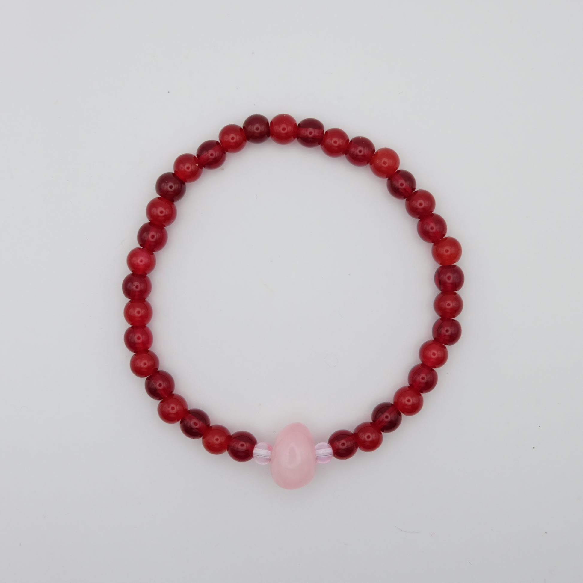 Beaded bracelet with red beads and a pink bead on a white background
