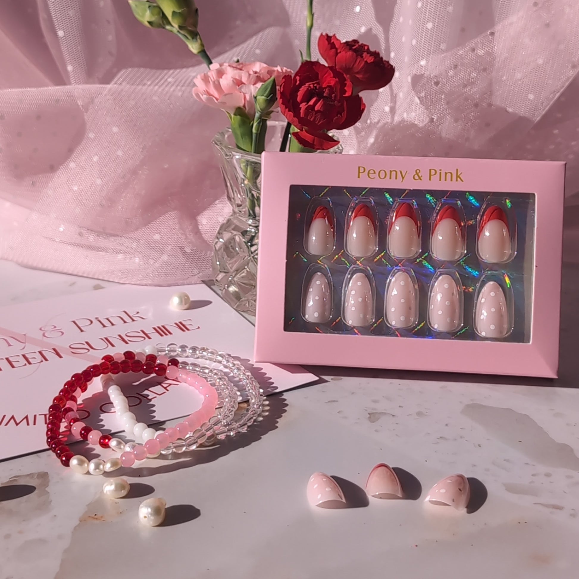 Set of false nails in a pink box with flowers and jewelry on a light surface