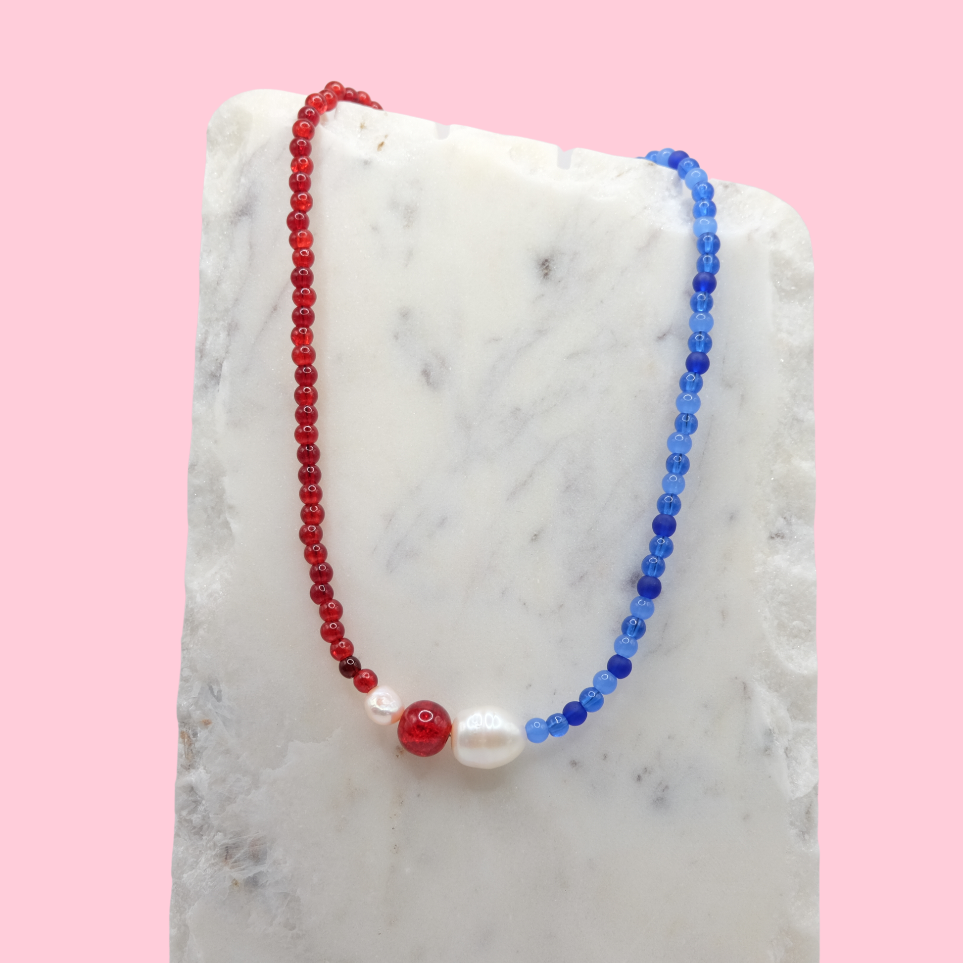 Necklace with red, blue, and white beads on a marble surface with a pink background