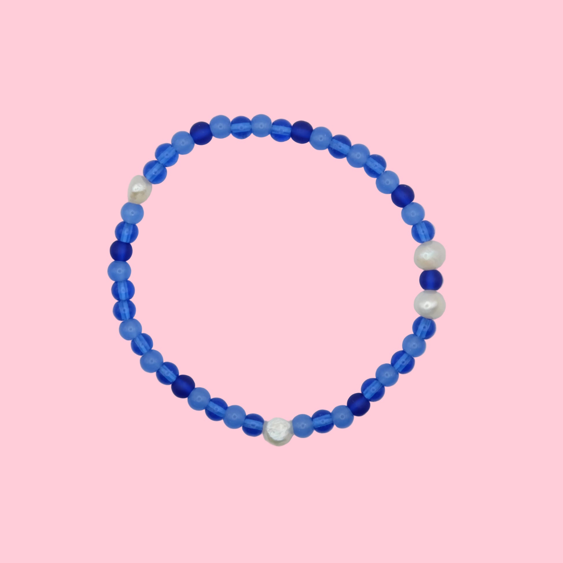 An elastic beaded bracelet composed of 4mm glass beads in blue tones -featuring small freshwater pearl accents, shown on a pink background.
