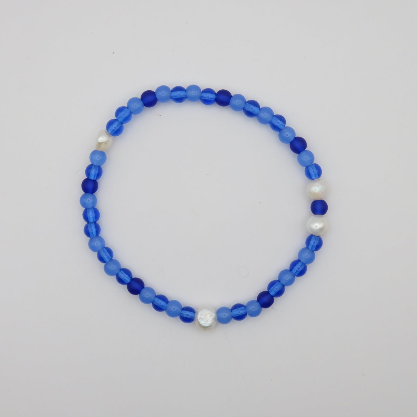 Blue beaded bracelet with white pearls on a light gray background