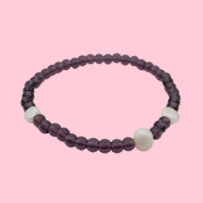 An elastic beaded bracelet composed of deep purple 4mm glass beads featuring freshwater pearl nugget accents, shown on a white background.